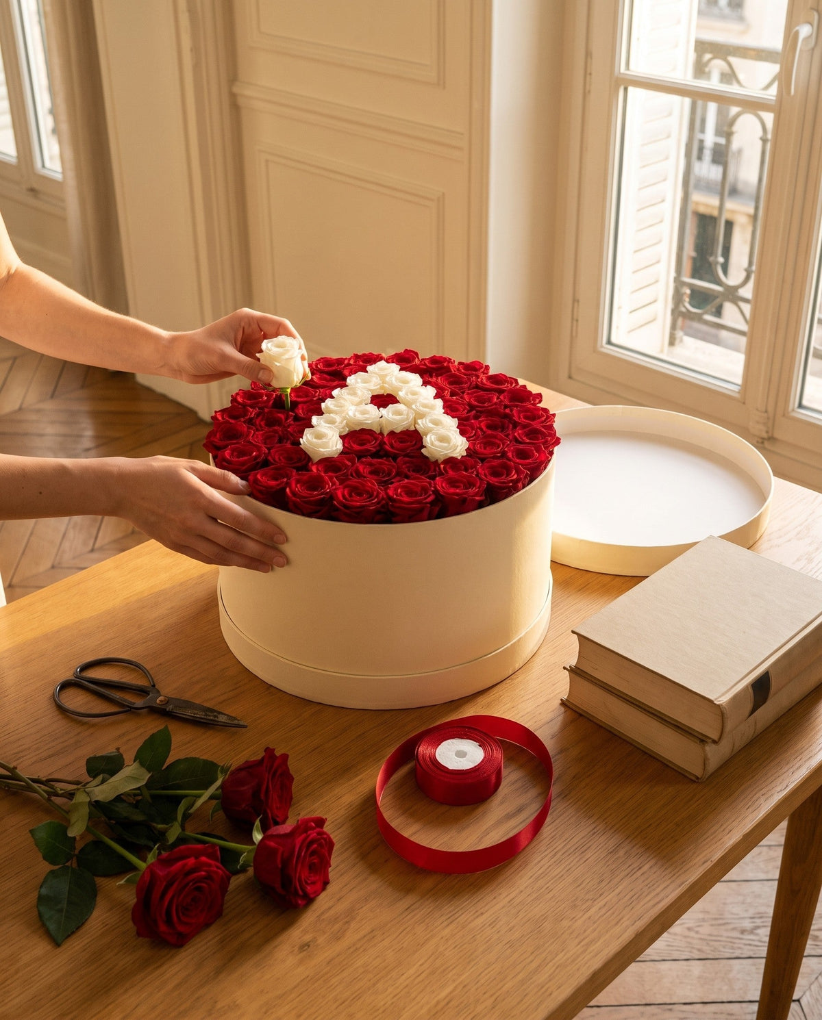 Des mains posent la dernière rose blanche d'une initiale dans une box de roses rouges, sur une table d'étudiante