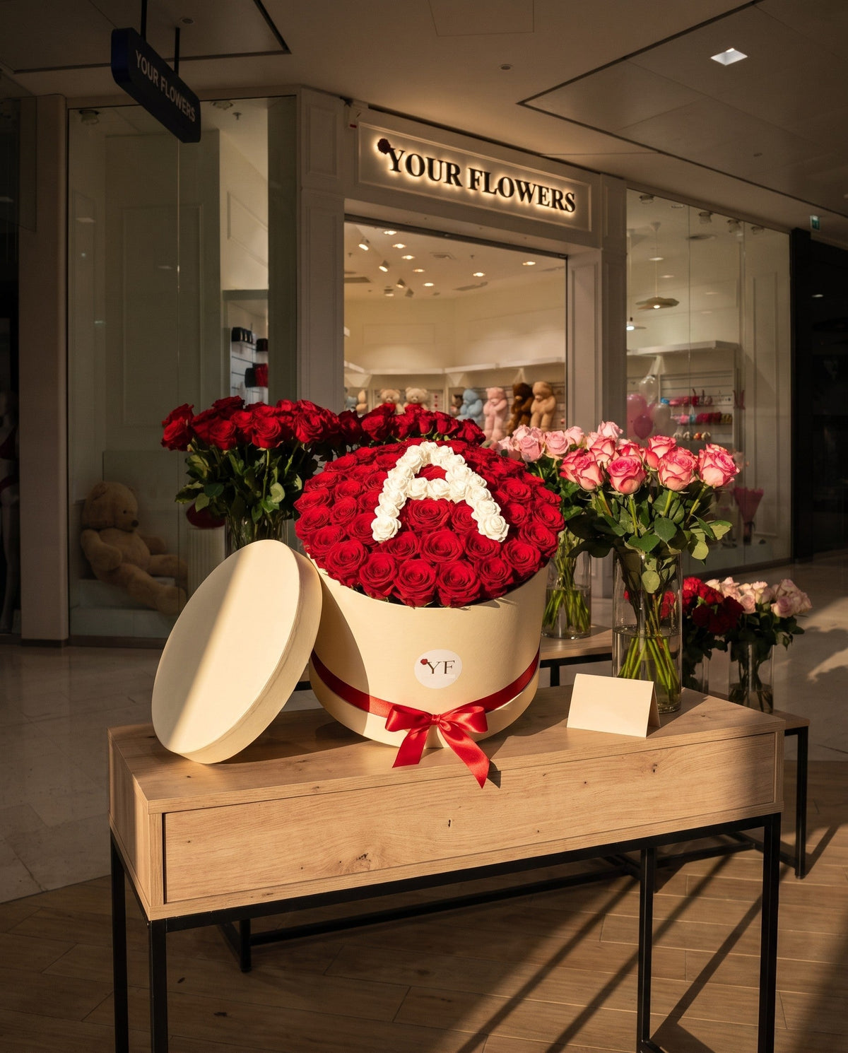 La box de roses rouges à l'initiale en roses blanches, exposée sur la console d'une boutique Your Flowers