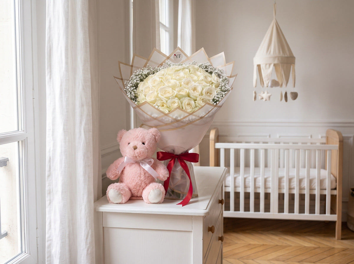 Un bouquet de roses blanches et un nounours rose posés sur la commode d'une chambre de bébé