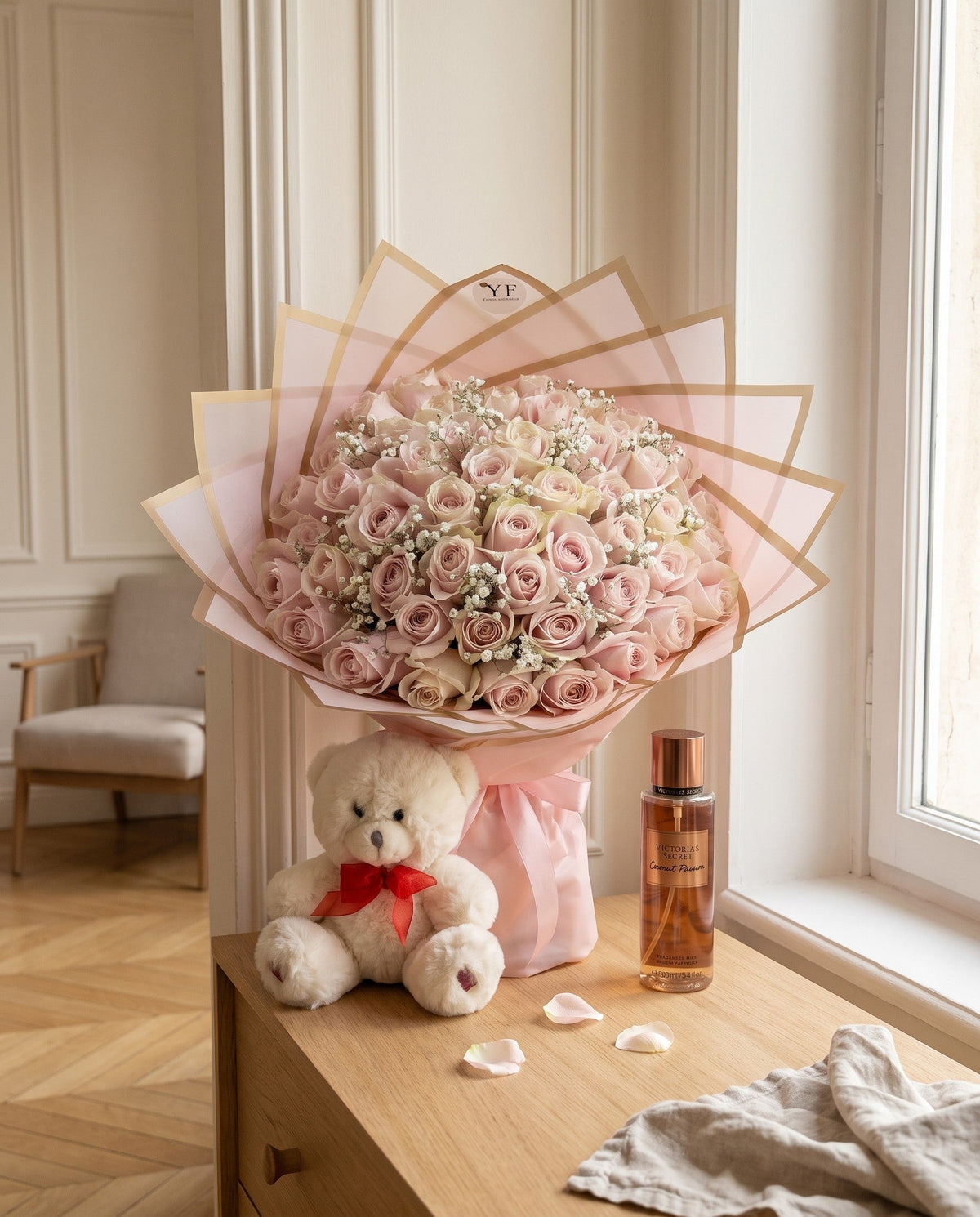 Un bouquet de roses roses, un petit nounours blanc et une brume parfumée réunis sur une commode